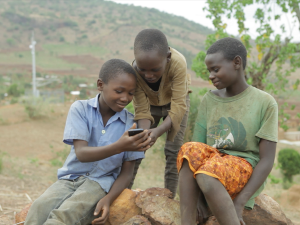 Three rural Kenyan community members using a smartphone together outdoors, symbolizing digital financial inclusion through mobile technology.