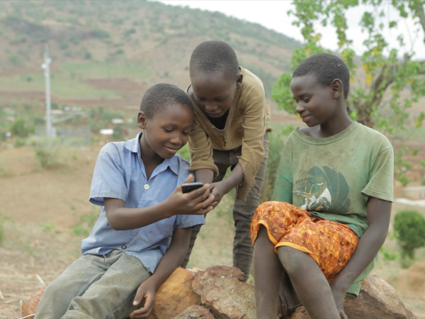 Three rural Kenyan community members using a smartphone together outdoors, symbolizing digital financial inclusion through mobile technology.